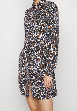 Frau trägt ein langärmliges, tailliertes Hemdblusenkleid mit einem mehrfarbigen abstrakten Leopardenmuster in Schwarz, Orange und Marineblau.