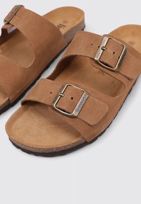 Sandalias de ante marrón con dos correas ajustables que incluyen hebillas de metal, una plantilla de corcho contorneada y una suela de goma texturizada.