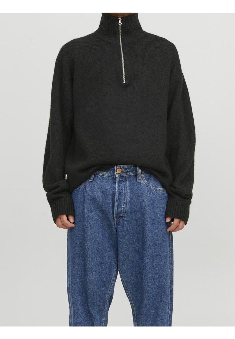 Ciemny dziany sweter z wysokim kołnierzem i półzamkiem. Połączony z luźnymi, niebieskimi dżinsami. Sweter z prążkowanymi mankietami i dołem.