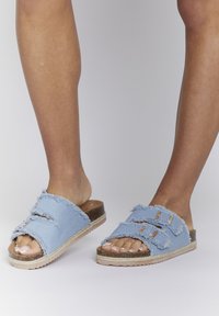 Sandalias deslizantes de denim azul claro con bordes deshilachados, diseño de doble tira y suela texturizada con un acento de fibra natural.