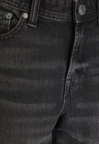 Close-up van zwarte spijkerbroek met voorzak, riemlus, metalen knoop en klinknagels.