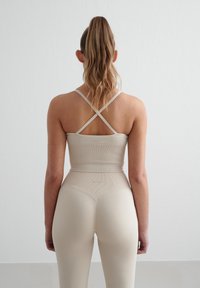 Beige sporttop met gekruiste banden en high-waisted leggings. Beide hebben een gladde textuur en ribbeldetails bij de tailleband.