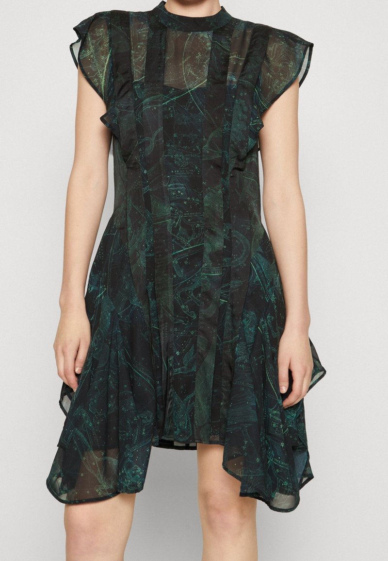 Robe noire transparente avec motif céleste vert, manches courtes volantées, col montant et ourlet asymétrique portée par une personne debout.