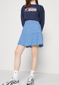 Sinili mabilog na palda na may maluwag na hem, na ipinares sa navy na sweatshirt na may logo ng 'TOMMY'. Kompletado ang hitsura ng mga pilak na athletic shoes.