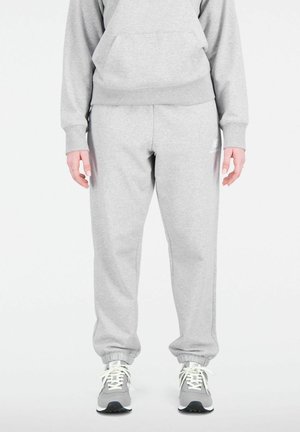 Graue Sweatpants aus weichem Stoff mit einem elastischen Bund und Bündchen, kombiniert mit grauen Sportschuhen mit weißen Schnürsenkeln.