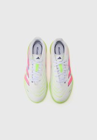 Des chaussures de sport blanches avec des accents verts et roses, présentant un design épuré, une surface texturée et des lacets contrastés.