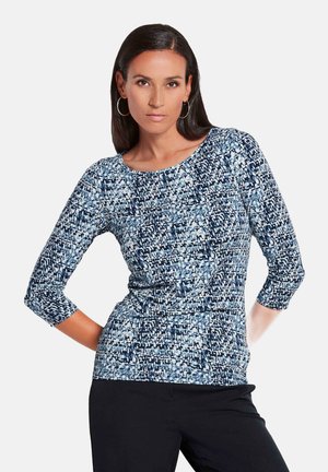 Haut à manches longues bleu et blanc à motifs, avec un col rond et une coupe ajustée, présentant un tissu légèrement texturé.