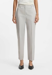 Lichtgrijze, op maat gemaakte broek met plooien, voorzien van een platte voorkant, ceintuurlussen en een cropped enkel lengte. Gecombineerd met zwarte schoenen met een spitse neus.