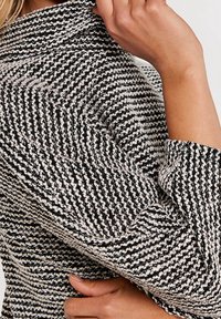 Tissu texturé en noir et blanc avec un motif à rayures, présentant une coupe ajustée et un col prolongé. La manche comporte un revers roulé.