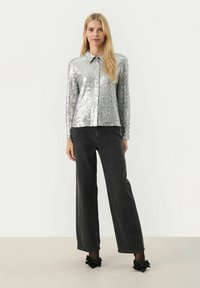 Sølvglitrende langærmet top med krave, parret med højtaljede sorte wide-leg jeans og sorte hæle med sløjfe pynt.