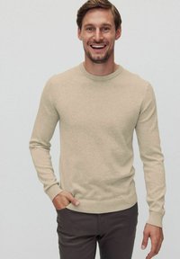 Beige stickad tröja med långa ärmar och rund halsringning, med en mjuk yta samt ribbade muddar och nederkant. Bärs med mörka byxor.