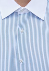 Chemise rayée vertical bleu et blanc avec col blanc et trois boutons visibles à l'avant.
