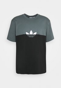Camiseta de hombre con un diseño de bloques de color; la sección superior es gris y la sección inferior es negra. Presenta el logo blanco de Adidas en el pecho.