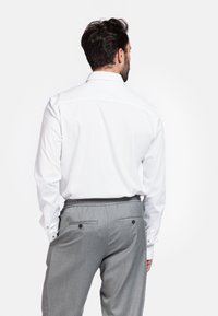 Witte lange mouw shirt met een kraag met knopen, gecombineerd met grijze pinstripe broek met elastische tailleband en twee achterzakken met knopen.