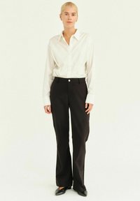 Camicia bianca con colletto, abbinata a pantaloni neri con una leggera lucentezza e chiusura anteriore a bottoni. Design slim-fit.