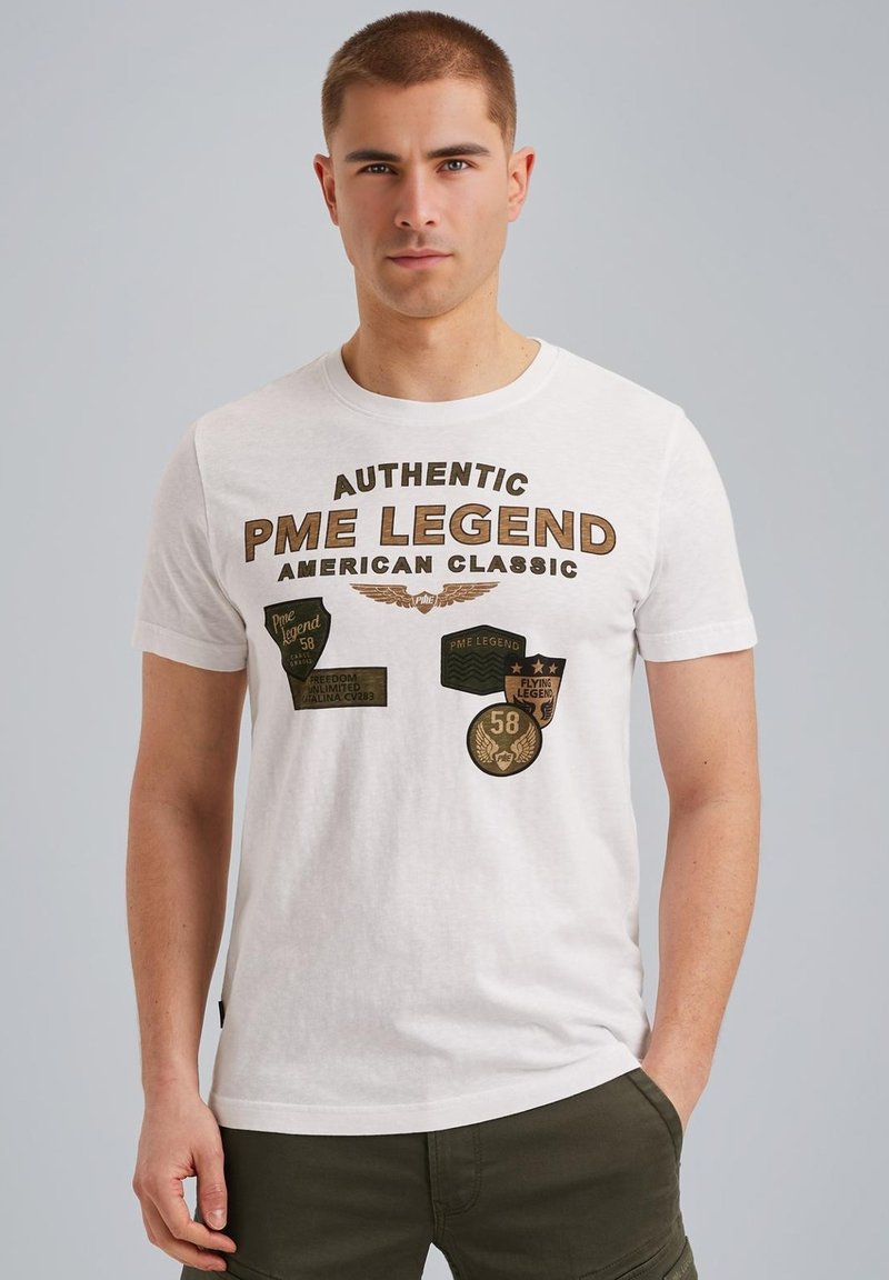 T-shirt en coton blanc avec des patches imprimés et du texte marron, arborant la marque "PME Legend" et des détails subtils sur le devant.