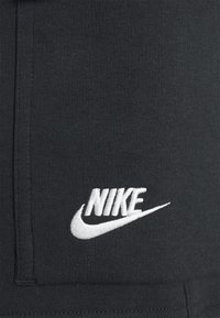 Svarta bomullsbyxor med texturerad finish och vitt broderat Nike-logotyp på vänster lår. Enkelt design, inga ytterligare mönster eller accenter.