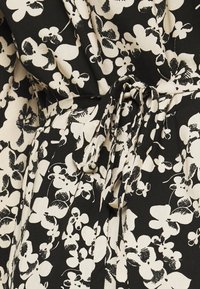 Svart tyg med vit blommig tryck som har oregelbundet formade blommor, knutet i midjan med ett matchande tygbälte.