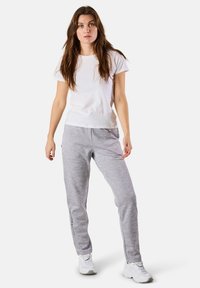 Valkoinen lyhythihainen t-paita ja harmaat collegehousut sivutaskuilla; juoksutyyli, pehmeä materiaali ja painettu logo lahkeessa.