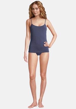 Giovane donna in piedi a piedi nudi che indossa una canottiera blu navy e biancheria intima abbinata su sfondo bianco.