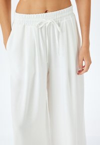 Witte wijde broek met elastische tailleband, verstelbaar trekkoord en zijzakken; gemaakt van lichtgewicht, gestructureerde stof.