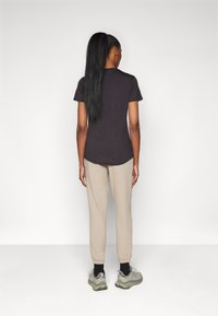 Schwarzes T-Shirt mit kurzen Ärmeln und abgerundetem Saum, kombiniert mit beigen Jogginghosen und grauen Sneakers. Langes Haar zu einem Pferdeschwanz gebunden.