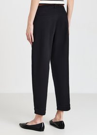 Pantaloni neri con vestibilità sartoriale, orlo risvoltato, tasche laterali e una cintura intrecciata. Tessuto liscio con una leggera lucentezza.