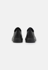 Black slip-on shoes with a smooth leather upper, rounded toe, and low rubber sole. Features a pull tab at the heel for easy wear.