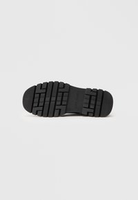 Fekete gumitalp, texturált felülettel, mély bordázattal és lekerekített szélekkel, az oldalán "STEVE MADDEN" felirattal.