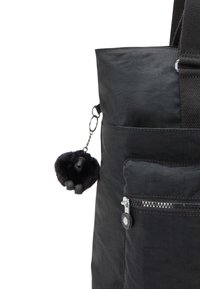 Borsa a spalla nera in tessuto a trama, con una tasca con zip e un portachiavi decorativo a forma di gorilla in peluche nero attaccato a un anello argento.