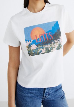 Biała bawełniana koszulka z kolorową grafiką przedstawiającą zachód słońca, góry i kwiaty, z napisem "LEVI'S" dużymi różowymi literami.