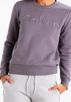 Grijze sweatshirt gemaakt van zachte stof, met een geborduurd logo in een lichter tint. Het heeft een ronde hals en ribbelboorden bij de mouwen en onderkant.