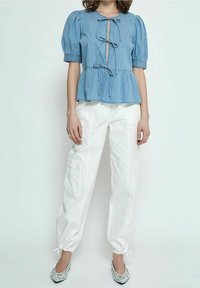 Top peplum in denim azzurro con maniche a sbuffo, chiusura anteriore con laccio e taglio centrale. Abbinato a pantaloni cargo bianchi e ballerine decorate.