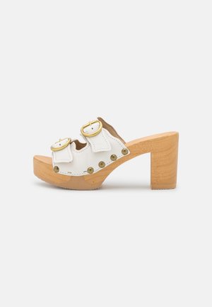 Sandalia de cuero blanco con tacón, hebillas dobles doradas, tachuelas de bronce, suela de plataforma de madera y tacón bloque, presentada sobre un fondo liso.