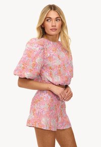 Ensemble en deux pièces rose à motifs floraux, comprenant un haut à manches bouffantes et un short assorti. Tissu texturé avec des motifs floraux colorés.