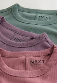 Three ribbed long-sleeve tops in green, purple, and pink. Each has a round neckline and a visible label with "NEXT" printed on it.