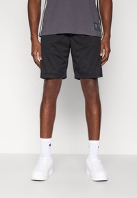 Μαύροι αθλητικοί σορτς από δίχτυ με ελαστική ζώνη μέσης, συνδυασμένοι με γκρι κοντομάνικο μπλουζάκι και λευκά αθλητικά παπούτσια. Λευκές κάλτσες με ορατό λογότυπο.