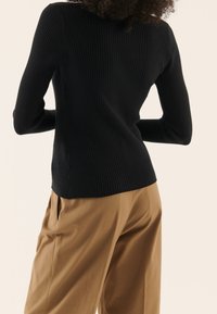 Pull noir côtelé à manches longues, avec une coupe ajustée et un ourlet arrondi, associé à un pantalon ample beige. Texture lisse, détails minimalistes.