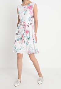 Blommig klänning i lätt tyg med korta ärmar, prydd med rosa och gröna mönster, en insydd midja med knytning och en utsvängd kjol.