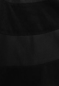 Svart mockafilter med en texturerad, perforerad sektion. Slät yta på överdelen. Matt utseende, lämplig för mångsidig styling.