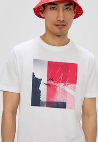 Witte katoenen T-shirt met een grafische print van rode en blauwe blokken, met duikers tegen een klifachtergrond. Korte mouwen, standaard pasvorm.
