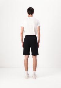 Black athletic shorts with a drawstring waist, side stripes, and a single back pocket. Paired with a plain white short-sleeve t-shirt.
