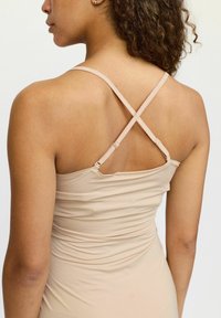 Camisă fără mâneci cu bretele încrucișate, confecționată dintr-un material neted. Prezintă un design ajustat și detalii pliate în spate.