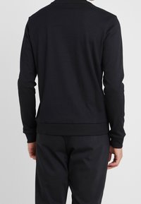 Camisa negra de manga larga con cuello redondo, hecha de una tela suave, con un diseño ajustado y dobladillos y puños acanalados.