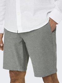 Shorts gris en tissu texturé et tissé. Poches latérales et coupe décontractée. Associés à une chemise en lin blanche.