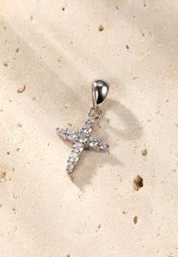 Zilveren kruis hanger versierd met heldere stenen, met een gepolijste textuur en een eenvoudige lus voor bevestiging. Geplaatst tegen een lichte ondergrond.