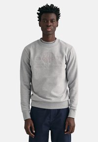 Grijze sweatshirt gemaakt van een katoenmix, met ribgebreide manchetten en onderkant, en met een reliëflogo op de voorkant. Gedragen over donkerblauwe broek.