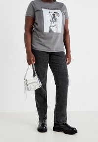 Harmaa t-paita, jossa on koira- grafiikka ja "COOL GIRL" -teksti, yhdistettynä mustiin farkkuihin, joiden koristeena on helmiä. Hopeinen ketjuhenkari ja mustat kengät.