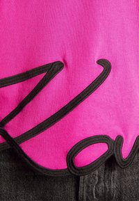 Fuchsia Stoff mit einem auffälligen schwarzen gestickten Design. Die Textur ist glatt mit einem leichten Glanz, ergänzt durch dunkles Denim-Material am unteren Rand.