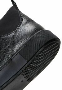 Czarny but typu slip-on wykonany z teksturowanej skóry, z gładką gumową podeszwą i wzorzystym uchwytem. Posiada elastyczne wstawki dla łatwego zakładania.